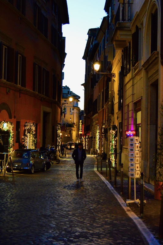 A dark alley in Italy with a man walking down it.